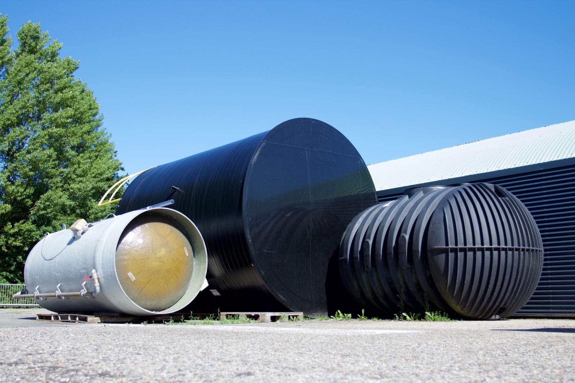 Grote kunststof opslagtanks en een ondergrondse regenwatertank op het buitenterrein van RLM