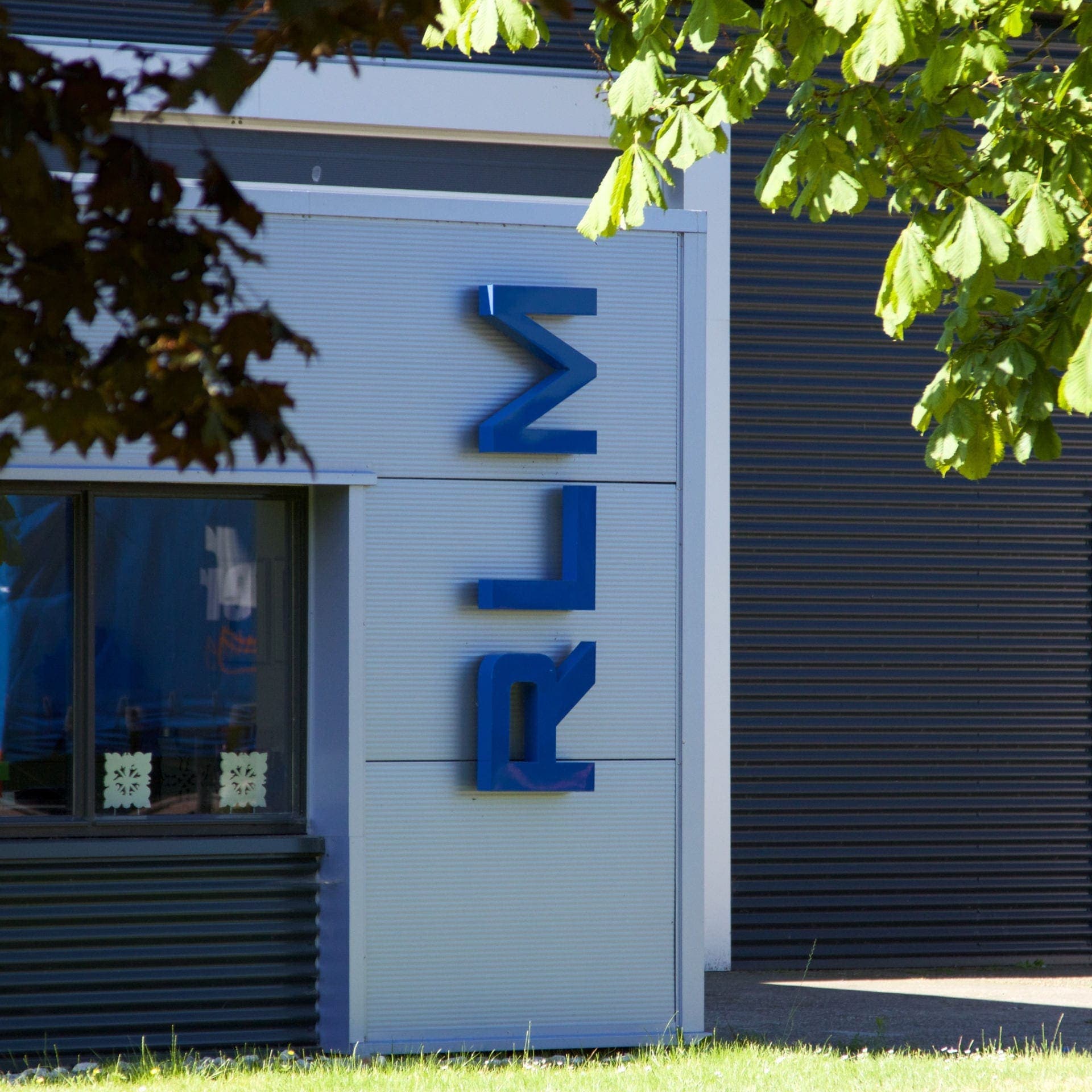 De blauwe letters RLM op de gevel van het bedrijfspand, onder een kastanjeboom