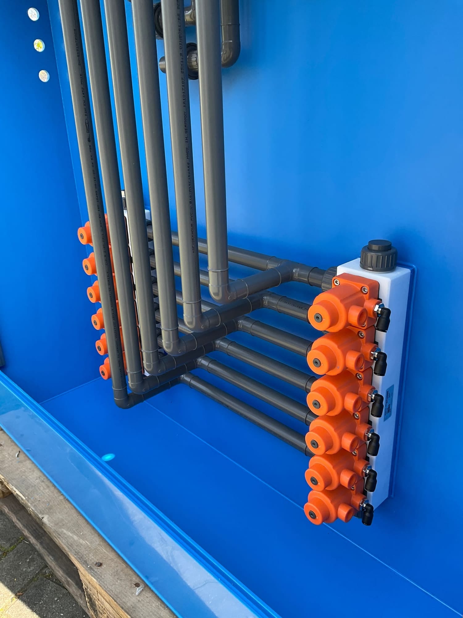 Op locatie gemonteerd PVC-leidingwerk met oranje afsluiters tegen de blauwe wand van een installatie