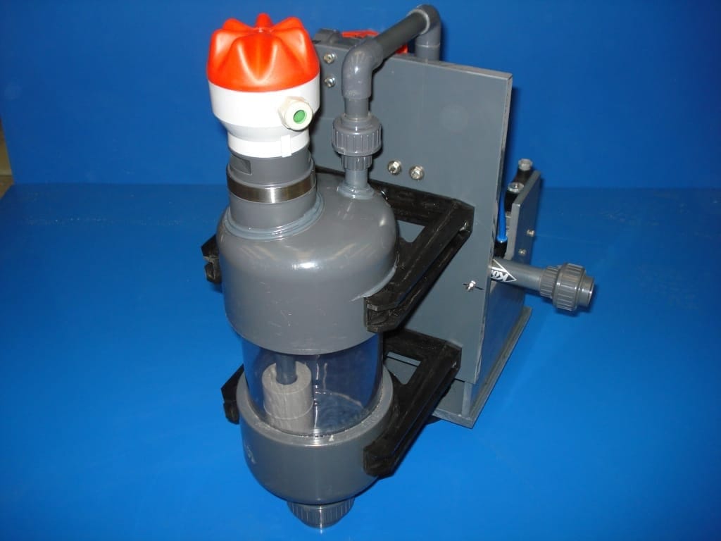 Automatisch hevelvat van grijs PVC met kijkglas en oranje sensorkap, gemonteerd in een zwarte beugel op een steunplaat