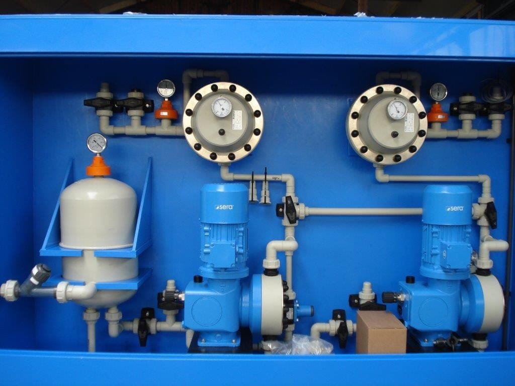 Binnenzijde van een doseerkast: twee sera-doseerpompen met pulsatiedempers, manometers en wit PVC-leidingwerk in een blauwe kast