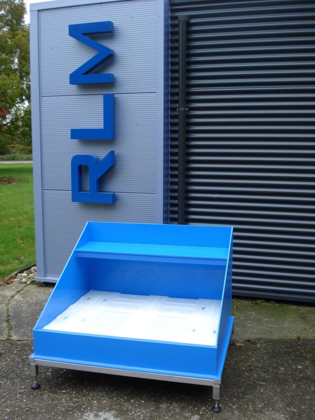 Blauwe kunststof lekbak met witte roostervloer en een opstaande achterwand, op een aluminium onderstel