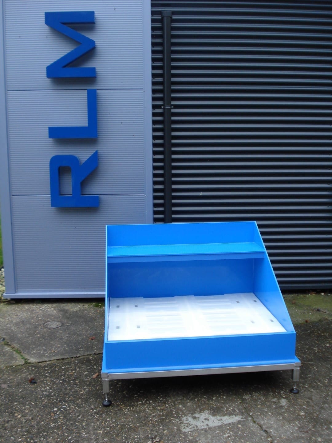 Blauwe kunststof opvangbak voor 200 liter-vaten met wit rooster en opstaande achterwand, voor de RLM-gevelletters