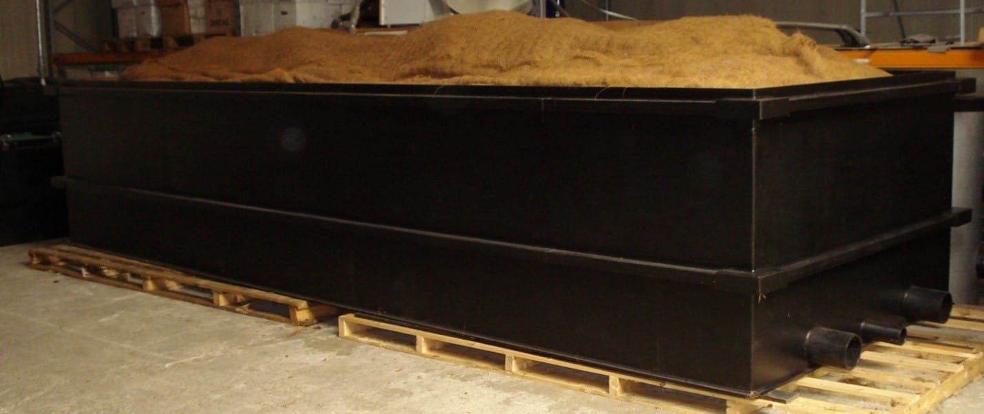 Zwarte rechthoekige opvangbak op pallets, afgedekt met een laag bruin biofiltermateriaal