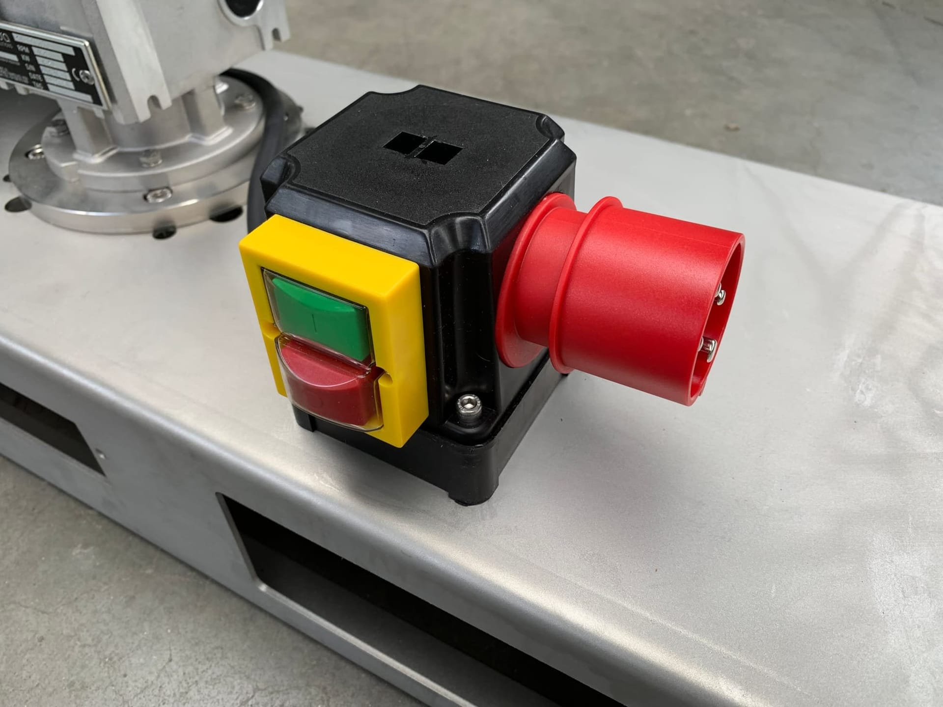 Schakelaar met groene start- en rode stopknop en een rode krachtstroomconnector op de rvs traverse van een IBC-mixer