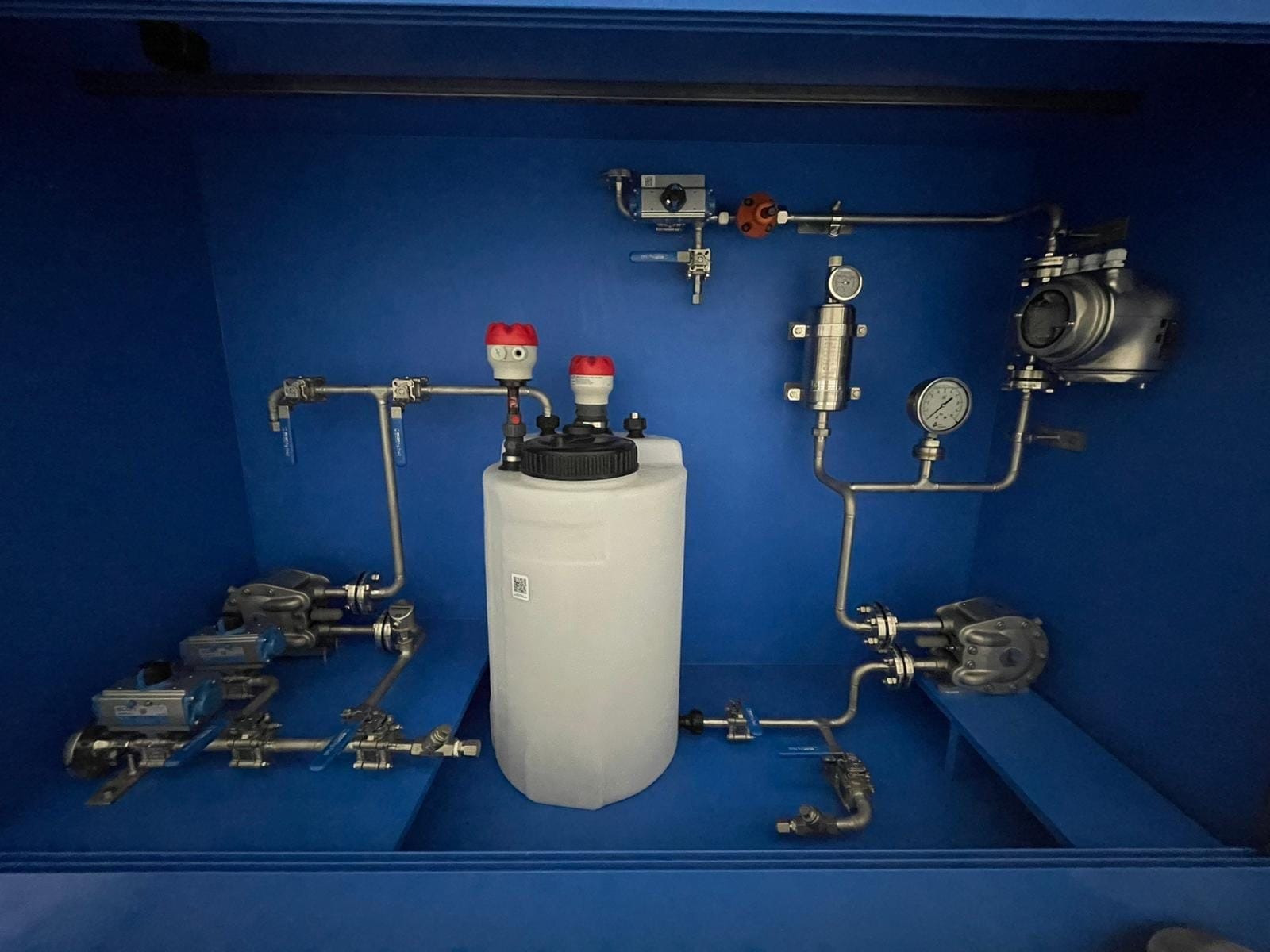 Doseerinstallatie in een blauwe opvangbak, met witte voorraadtank, twee pompen, pneumatisch bediende afsluiters en een manometer