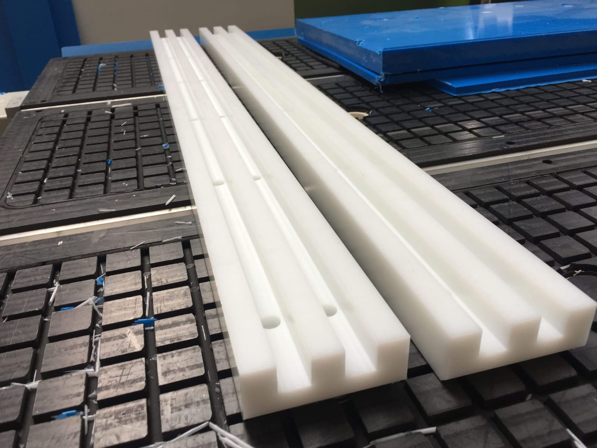 Twee gefreesde witte kunststof profielen met langsgroeven, op de vacuümtafel van de freesmachine