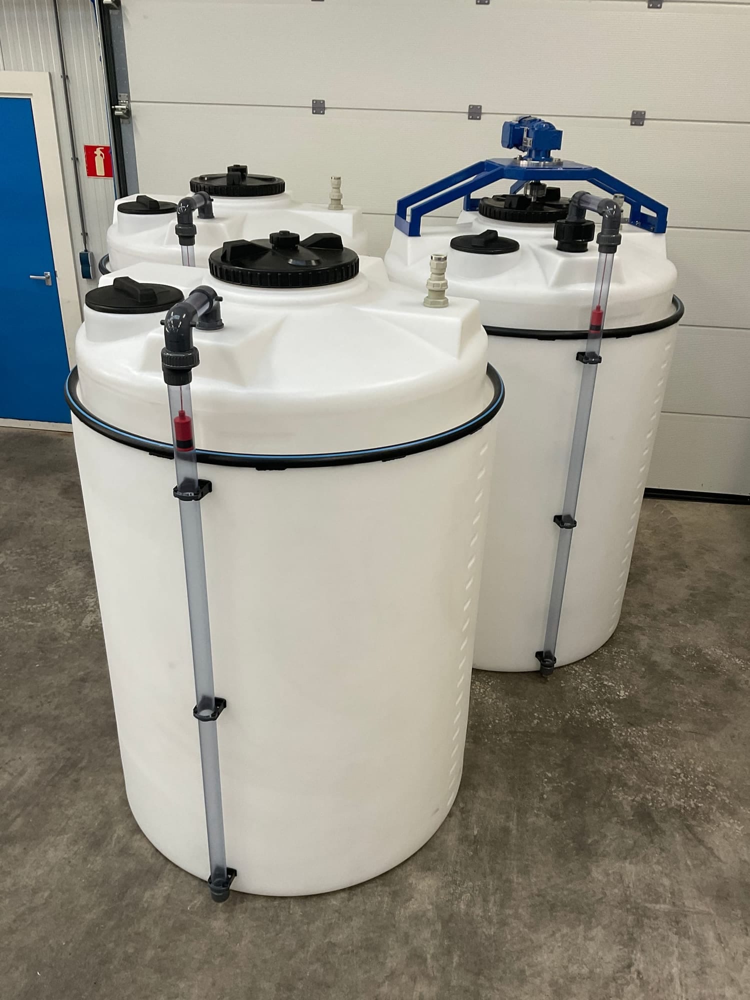 Drie witte PE-doseertanks in de werkplaats, elk met een peilglas langs de wand; op de achterste tank staat een blauw roerwerk