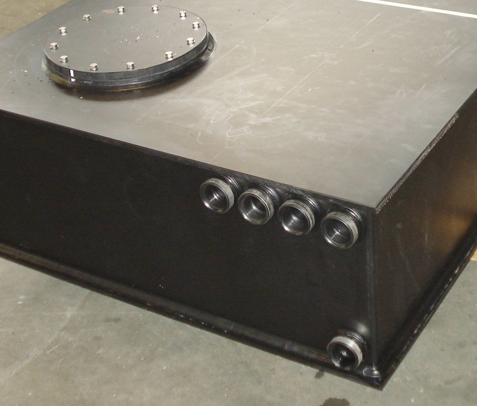 Hoek van een zwarte PE-tank met vier rvs schroefdraadaansluitingen op rij en een gebout mangatdeksel op het dak