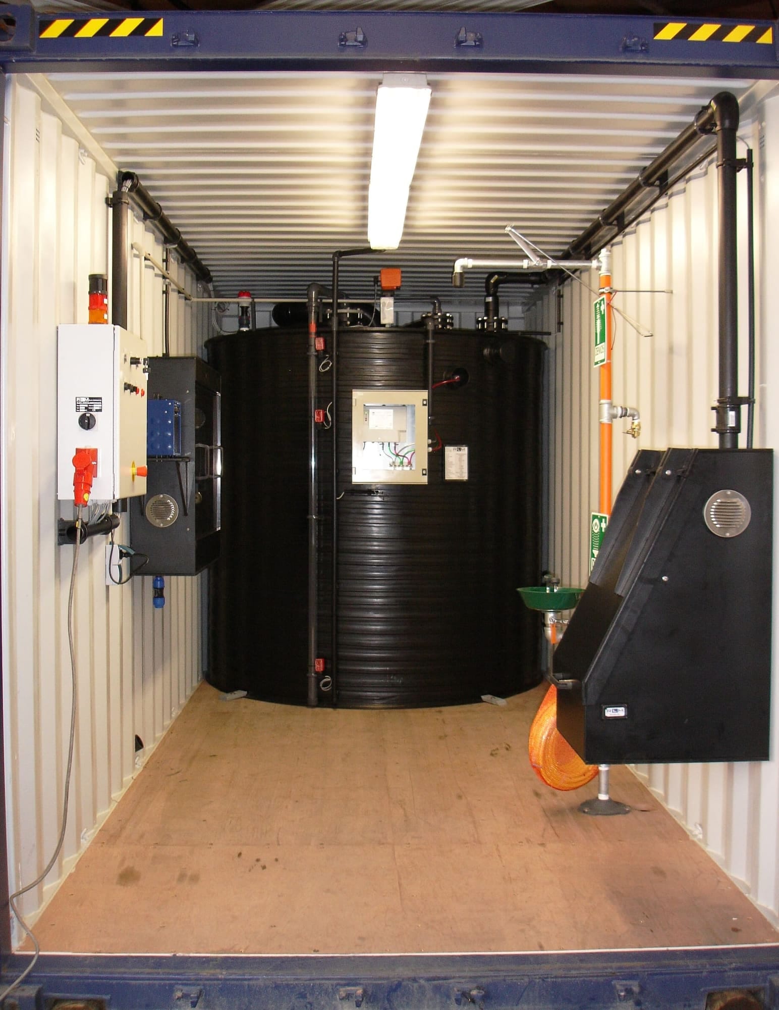 Zwarte ronde chemietank ingebouwd in een zeecontainer, met besturingskast, oogdouche en afzuigleiding