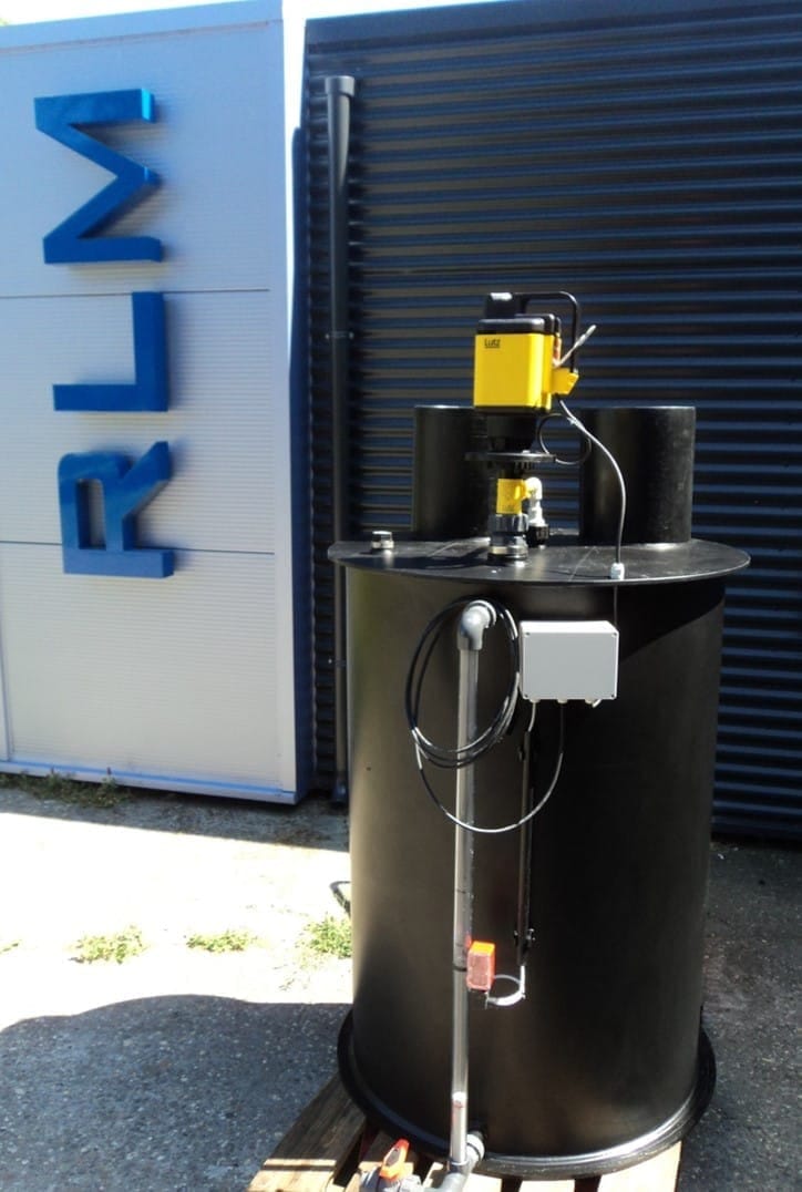 Zwarte ronde kunststof tank met een gele Lutz-motor en gaswasserkolom op het deksel, op het buitenterrein bij de RLM-gevelletters