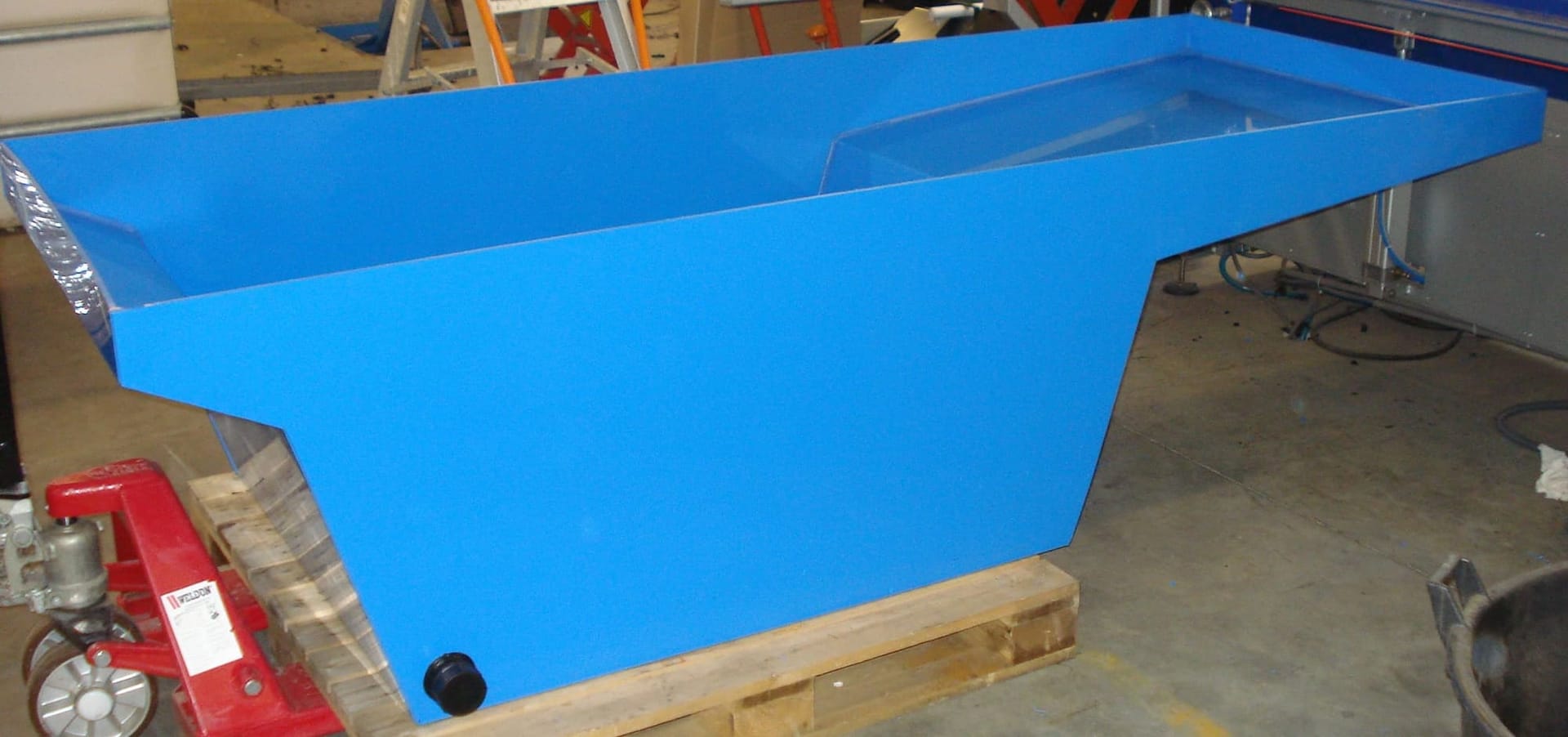 Blauwe kunststof opvangbak in maatwerkvorm met schuin aflopende zijkant, op een pallet in de werkplaats