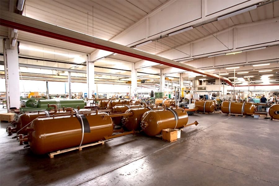 Productiehal met rijen bruin gelakte drukvaten voor pulsatiedempers op de vloer