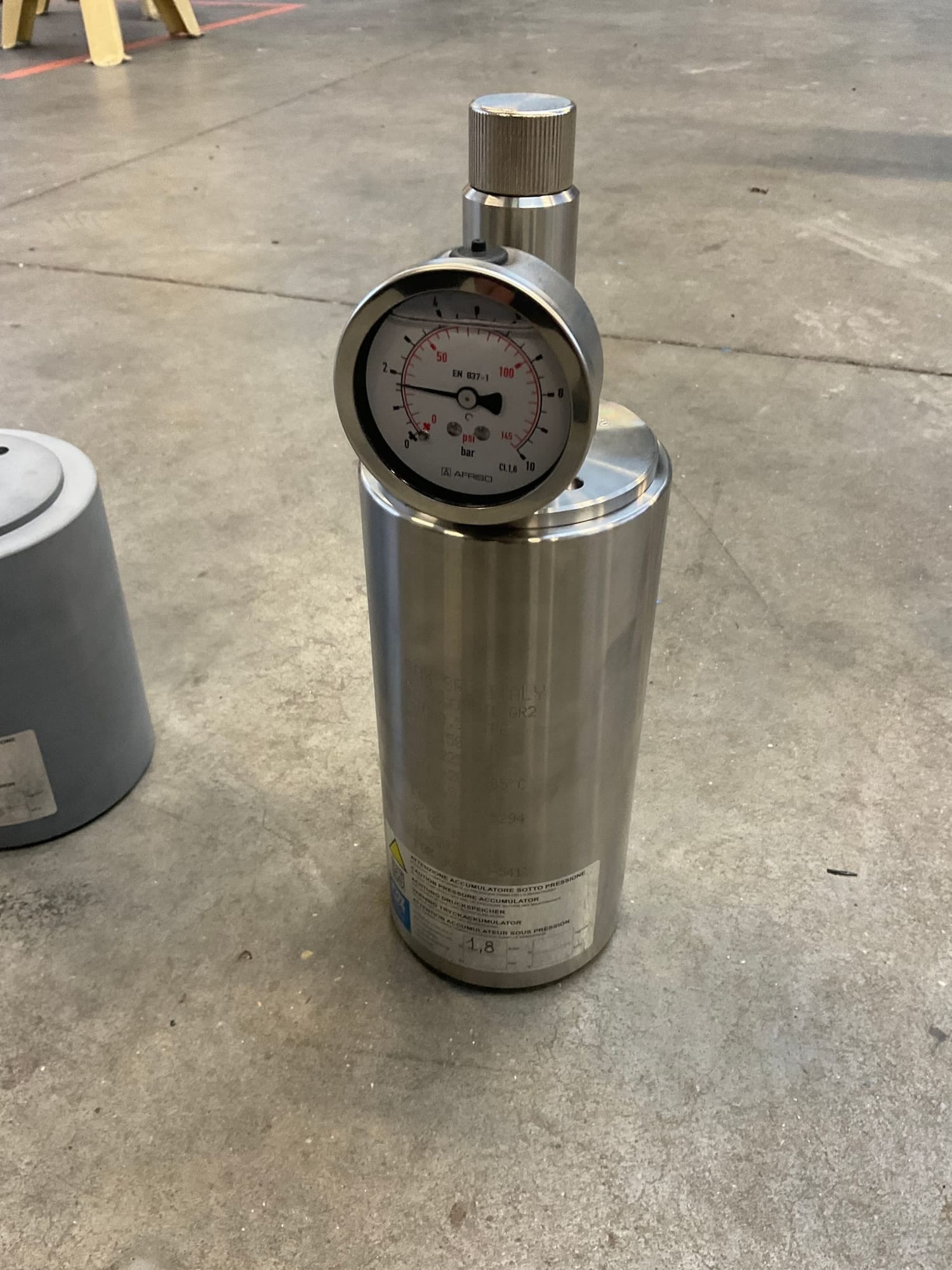 Rvs pulsatiedemper met manometer en vulventiel op de kop, met een waarschuwingssticker voor drukvaten op de mantel